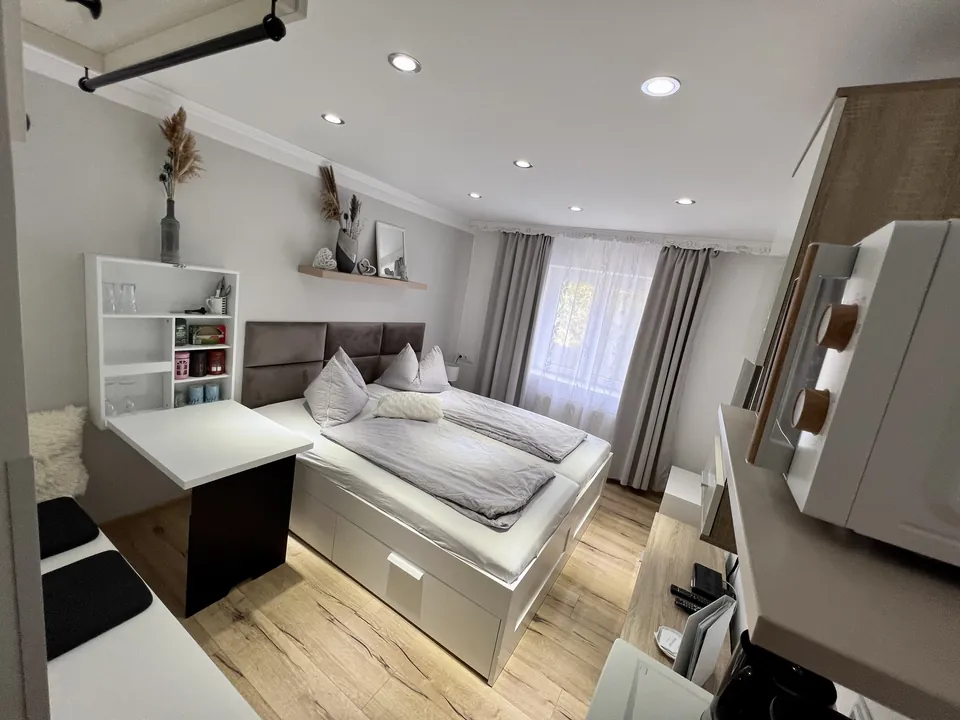 Blick in das Doppelzimmer mit Bett, Tisch und kleinem Kühlschrank