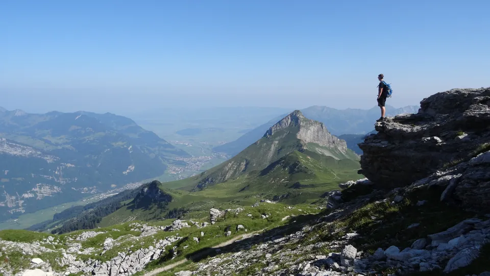 Wanderer auf einem Felsvorsprung mit Blick über die Berglandschaft